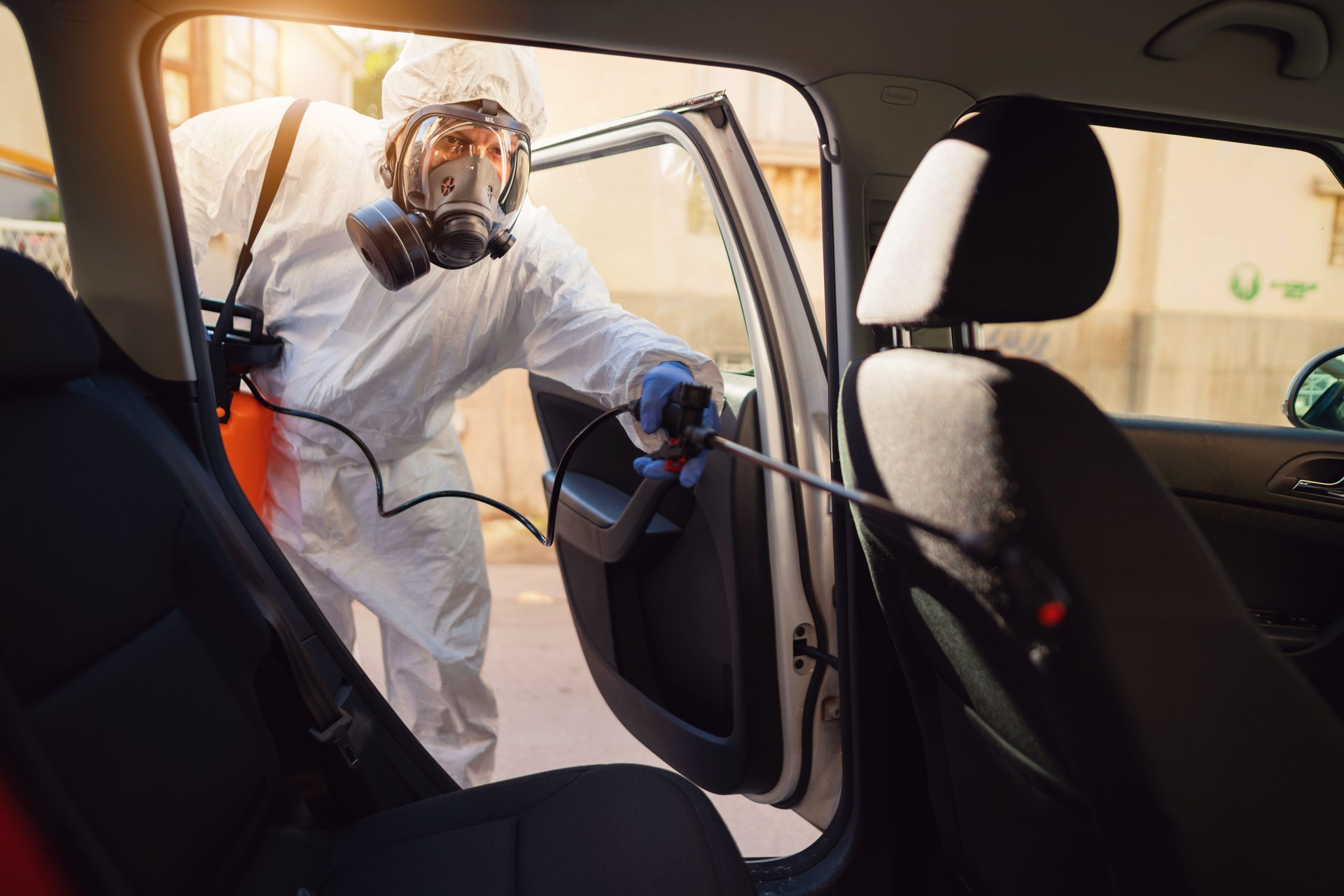 Man in protective suit and gas mask disinfect car